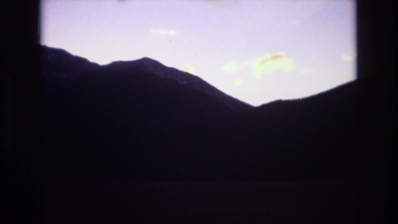 A dark mountain ridge appears in silhouette beneath a pale purple twilight sky in 1974 Colorado Springs footage.