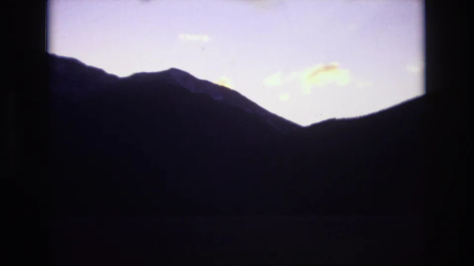 A dark mountain ridge appears in silhouette beneath a pale purple twilight sky in 1974 Colorado Springs footage.