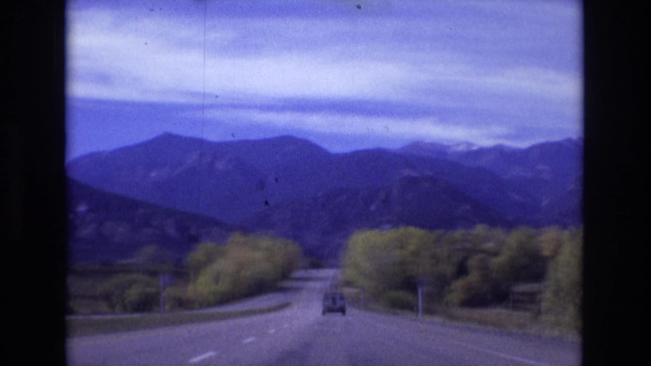 A small vehicle drives ahead on a two-lane road toward a distant mountain range.