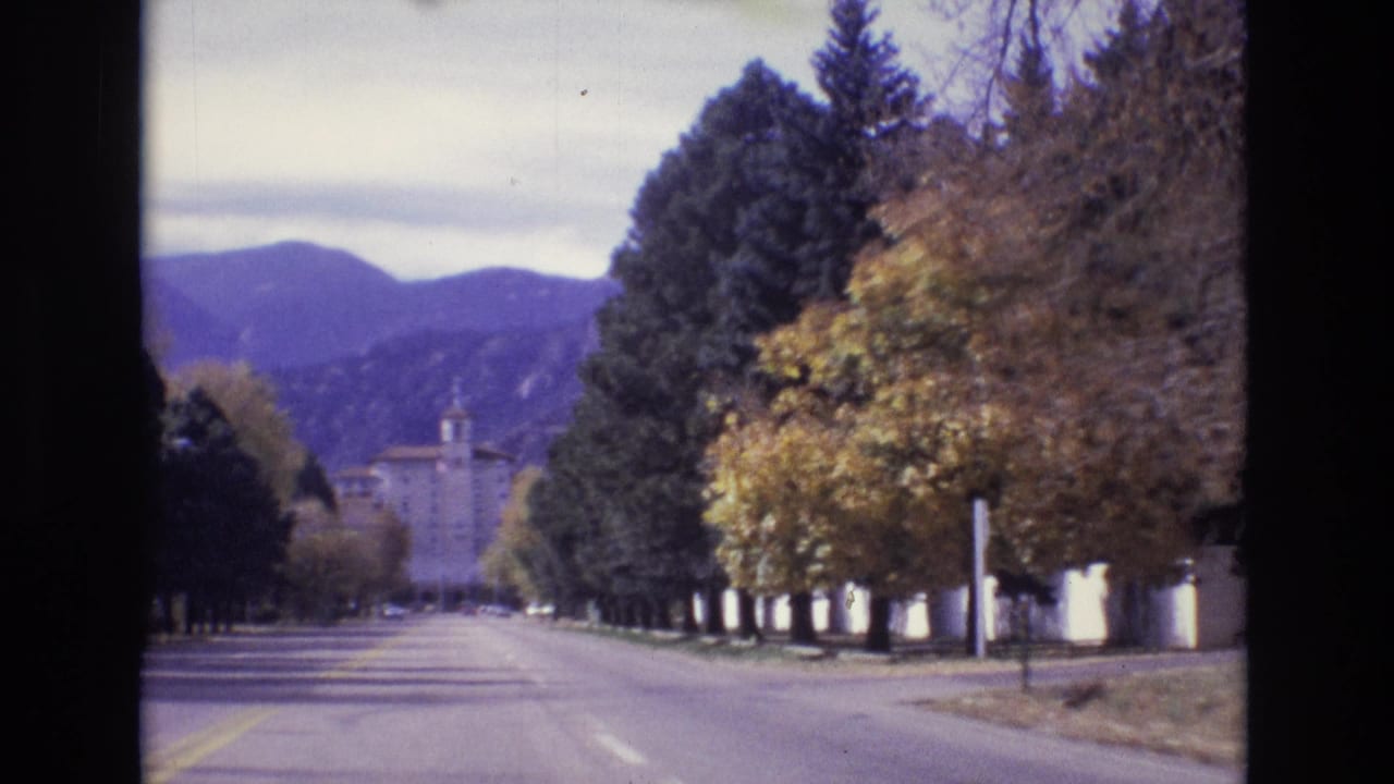 Tree-lined road leading toward a distant building and mountains.