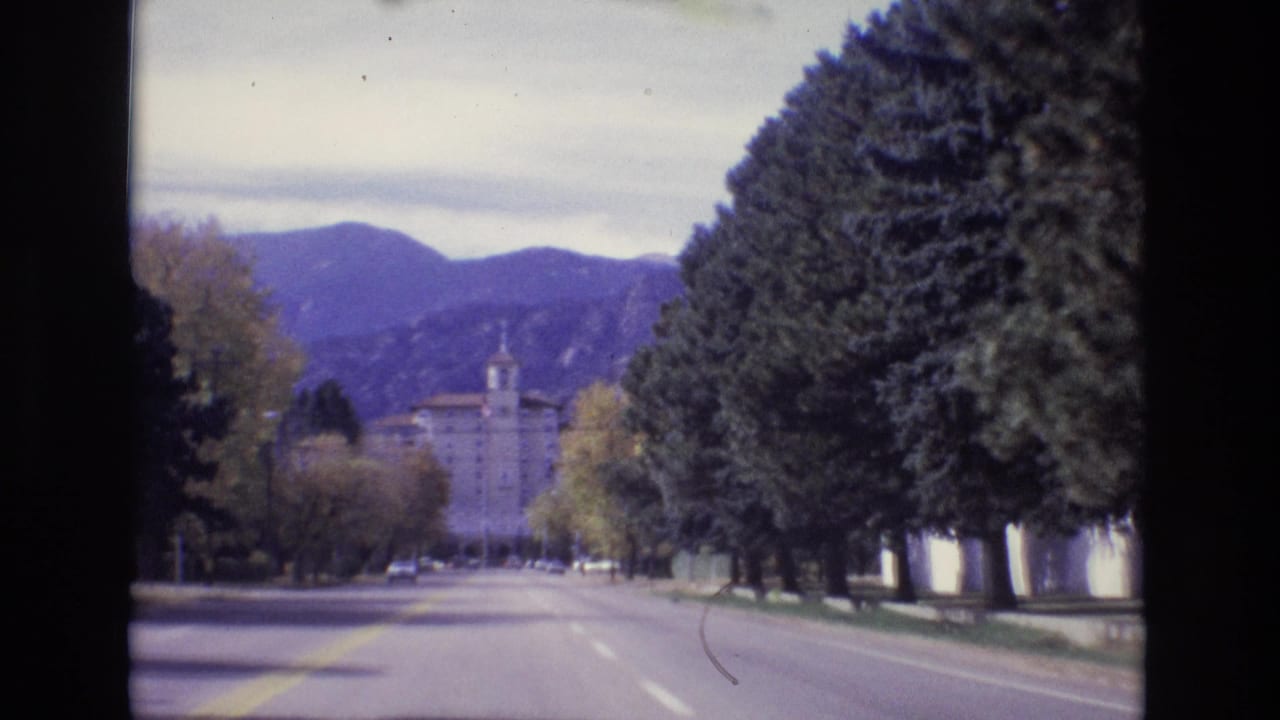 1974 Colorado Springs 8mm frame showing a forward drive along a broad tree-lined avenue with mountains and a towered institutional-looking building in the distance.