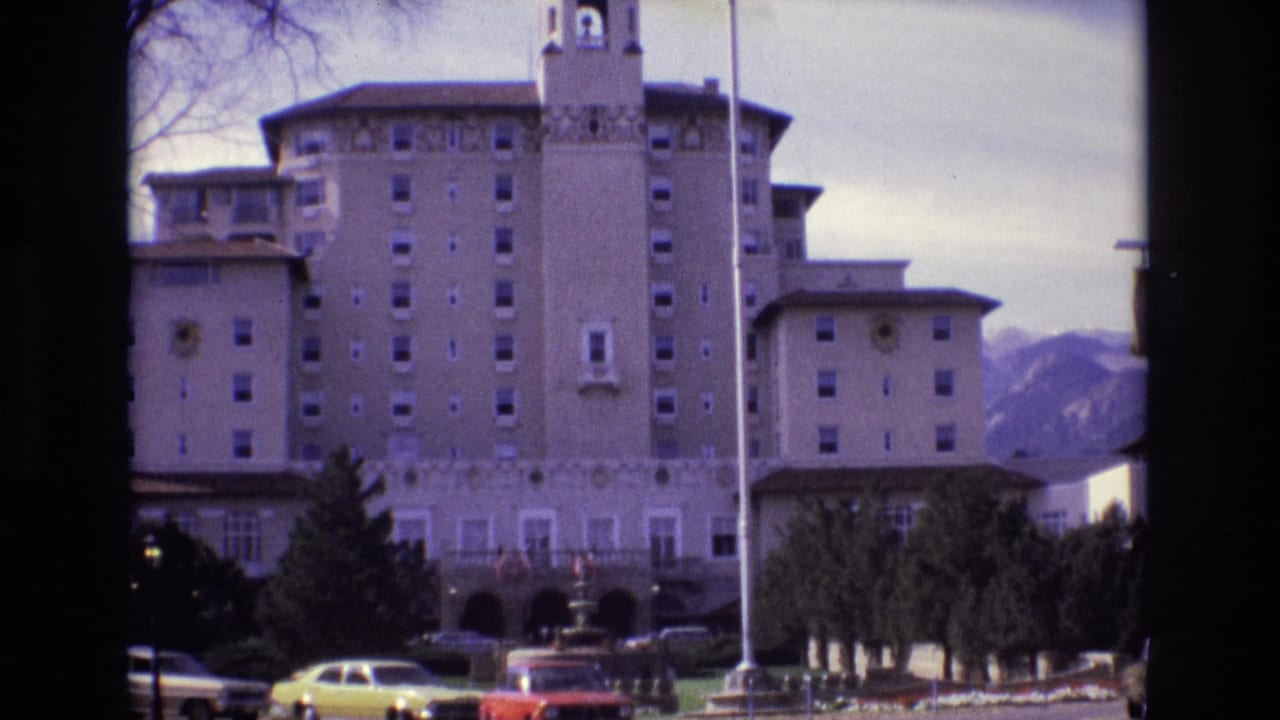 Hotel exterior framed by trees with parked cars and mountains visible in the distance.