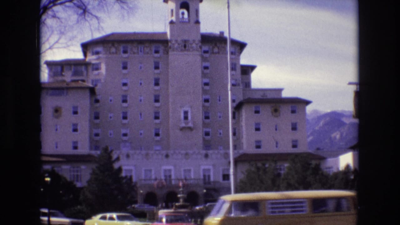 1974 Colorado Springs home-movie frame showing the Broadmoor Hotel facade and tower, mountains behind it, a flagpole, and period cars along the drive.
