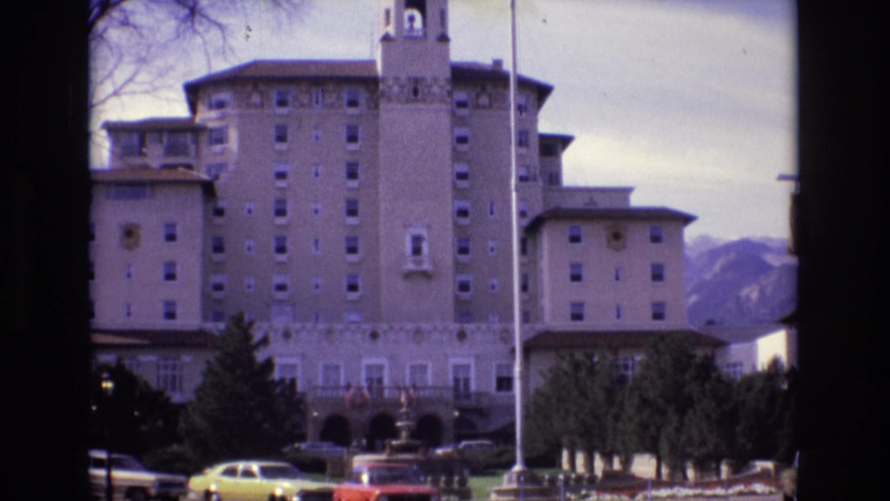 1974 Colorado Springs frame of the Broadmoor Hotel viewed from outside, with its central tower, mountain backdrop, flagpole, trees, and parked period cars.