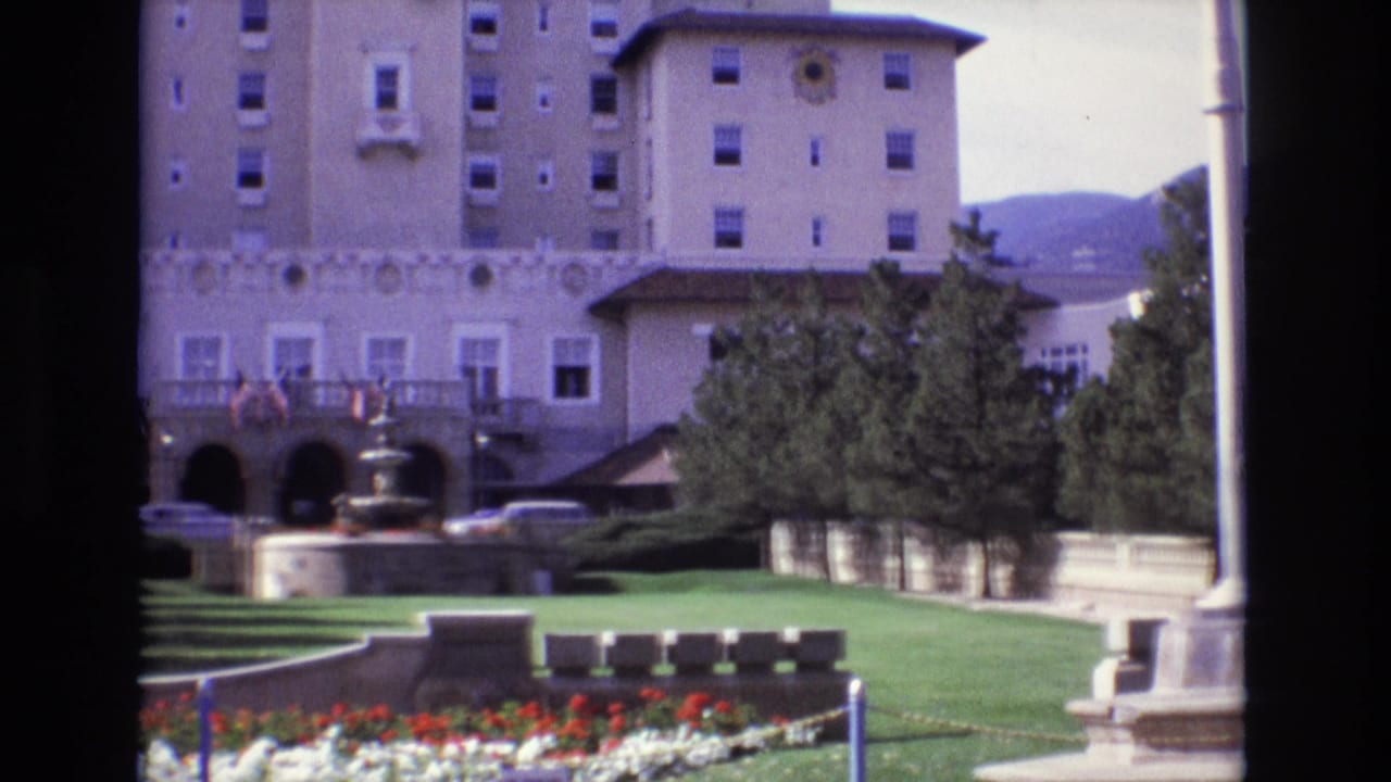 1974 Colorado Springs frame of the hotel grounds with arched entrance, fountain, formal lawn, trees, flower beds, and cars parked near the building.