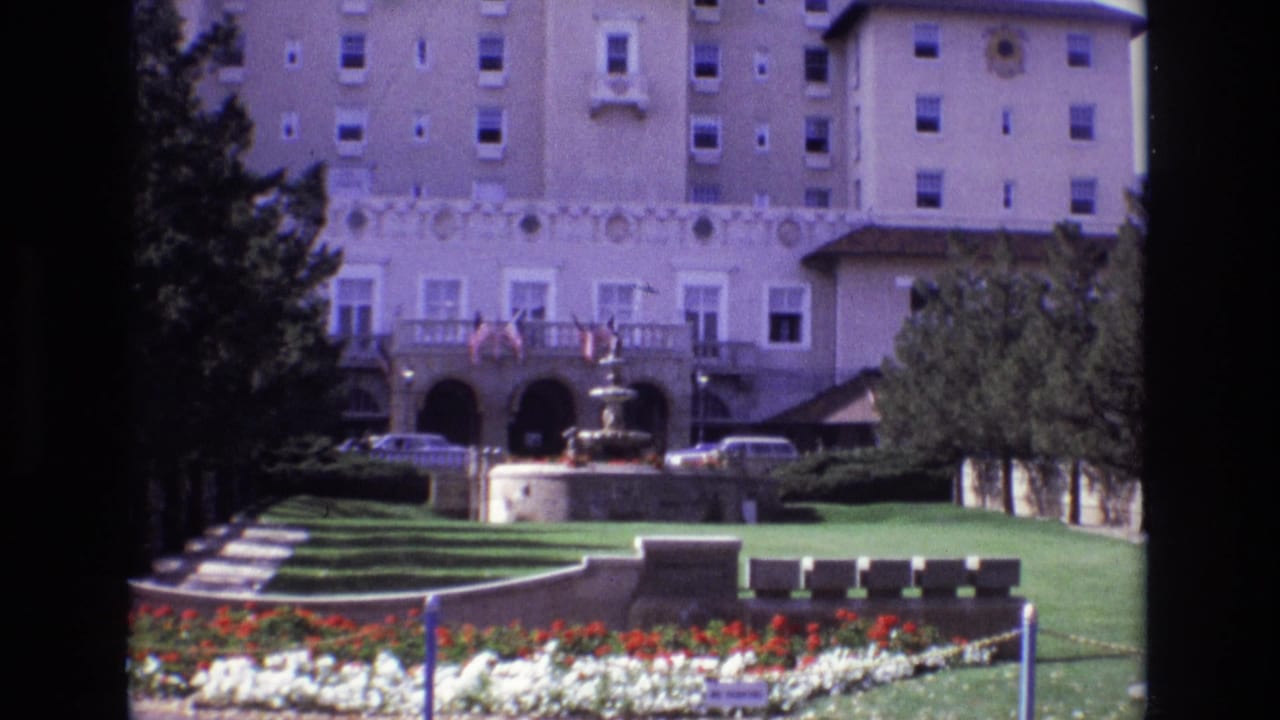 1974 8mm view of the Broadmoor Hotel grounds in Colorado Springs, with a fountain centered before lawns, flowerbeds, trees, and parked cars.
