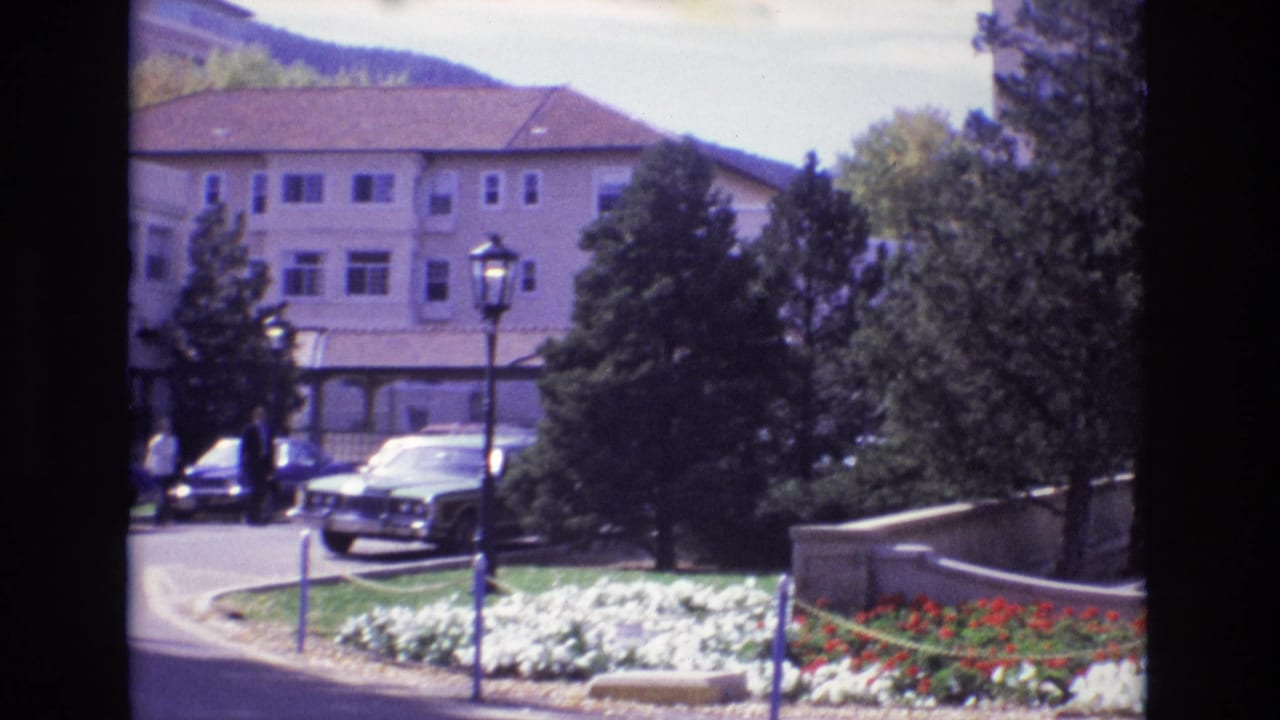Landscaped hotel grounds with flower beds, lampposts, trees, and parked cars.