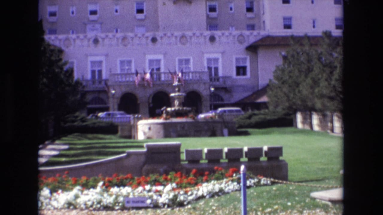 1974 8mm view in Colorado Springs showing the Broadmoor Hotel exterior with a central fountain, manicured lawn, flower beds, and parked cars near the entrance.