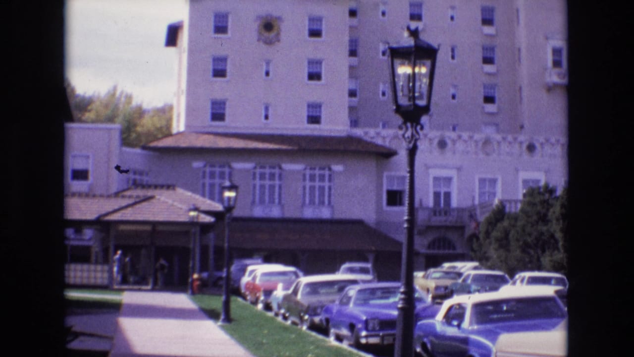 Hotel entrance drive with parked cars, lamppost, sidewalk, and tall building facade.