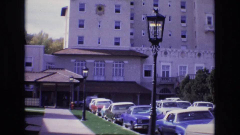 1974 Colorado Springs 8mm frame showing the Broadmoor Hotel driveway with several parked cars, a lamppost in the foreground, lawn, entrance canopy, and tall hotel facade.