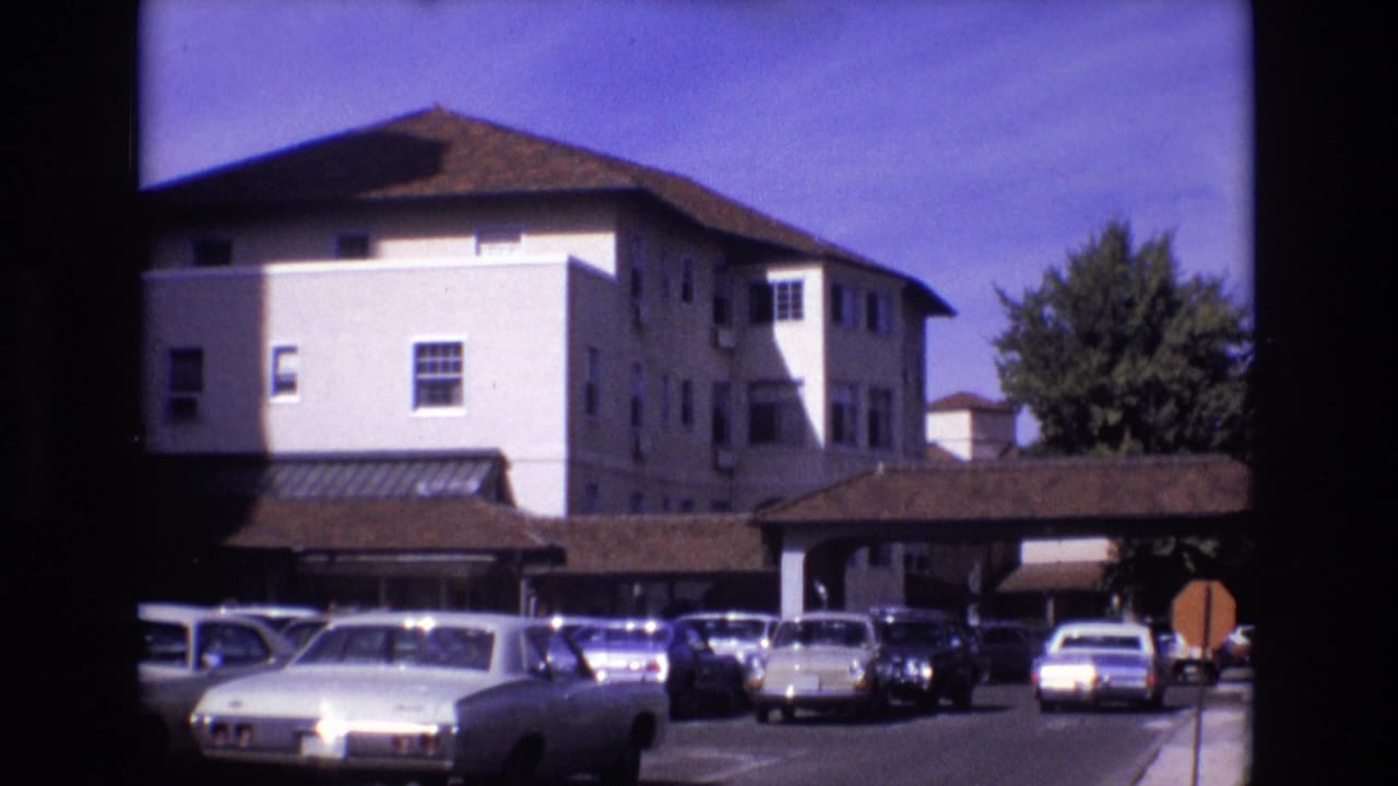 Parking area with vintage cars facing a white building and covered driveway.