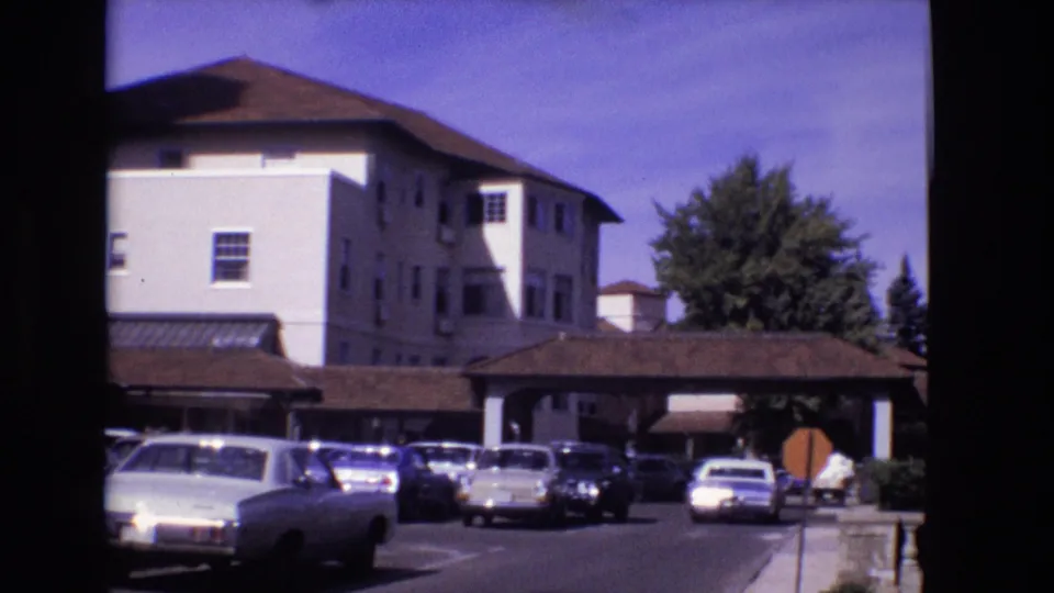 Visitor-shot 1974 Colorado Springs view of parked cars, a covered entry canopy, and the side of a white resort-like building.