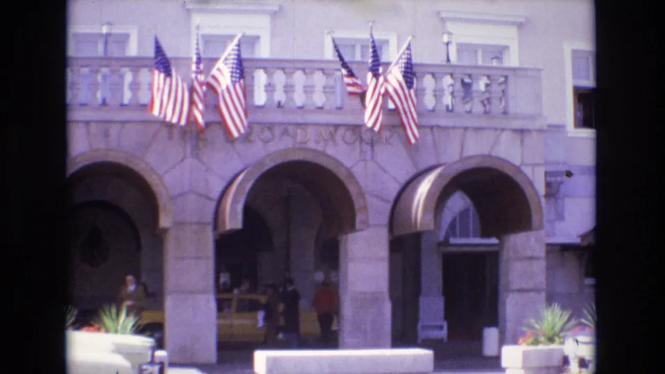 1974 Colorado Springs frame showing a stone arched facade with American flags, awnings, distant people, and Broadmoor lettering visible.