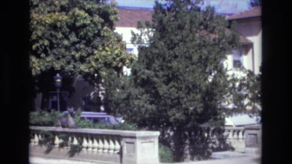 1974 Colorado Springs street view with a station wagon partly visible behind a stone balustrade, mature trees, a lamppost, and a light-colored building.