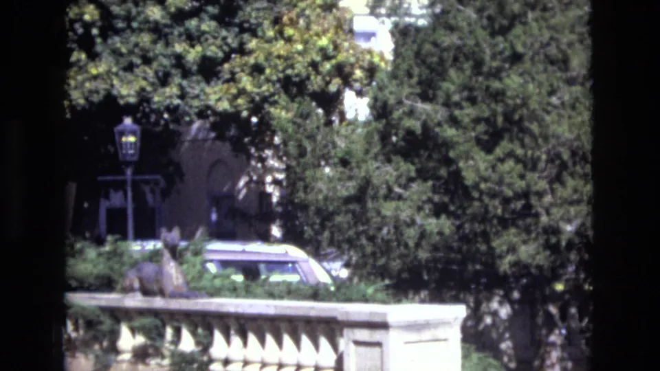 1974 Colorado Springs home-movie frame showing a stone balustrade, leafy trees, and a classic car near landscaped grounds.
