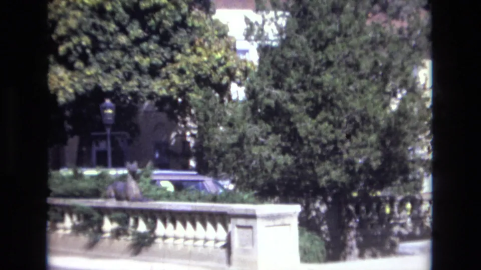 1974 Colorado Springs frame with a stone railing, dense trees, and a car partially obscured by the landscaped foreground.