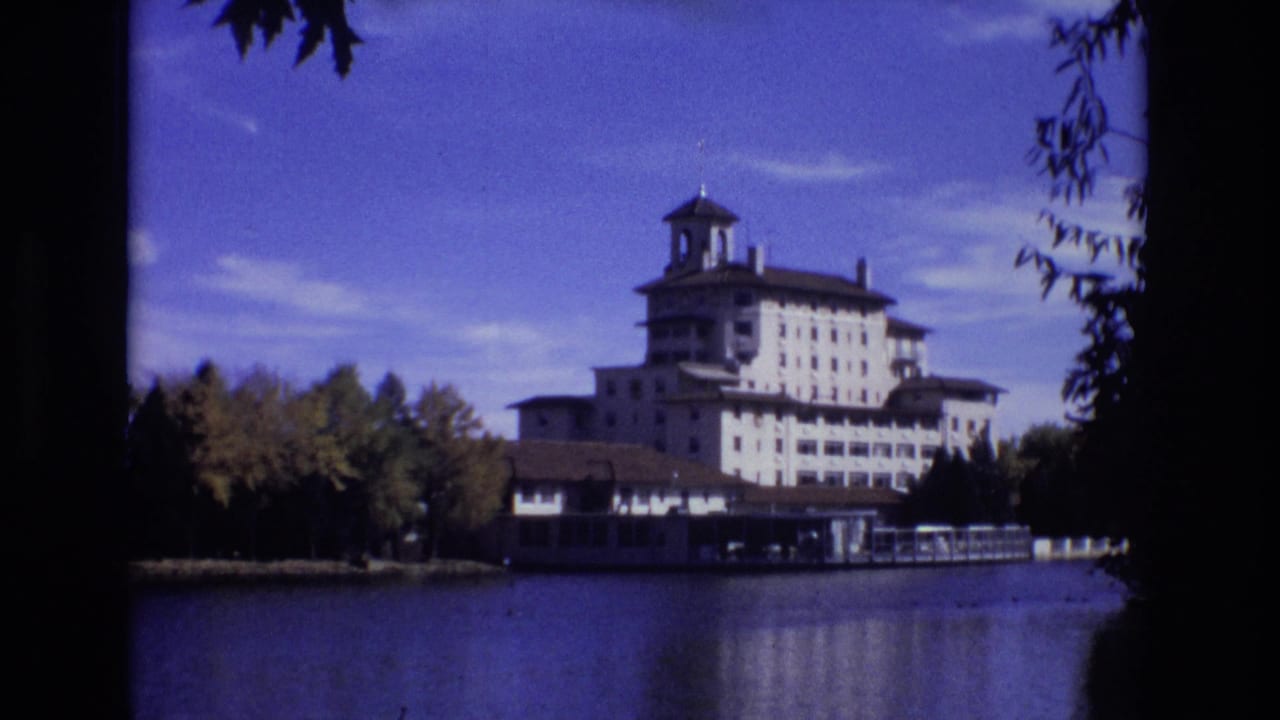The Broadmoor Hotel appears across the water in Colorado Springs, with its tower and pale facade visible beyond trees and a dark foreground frame.