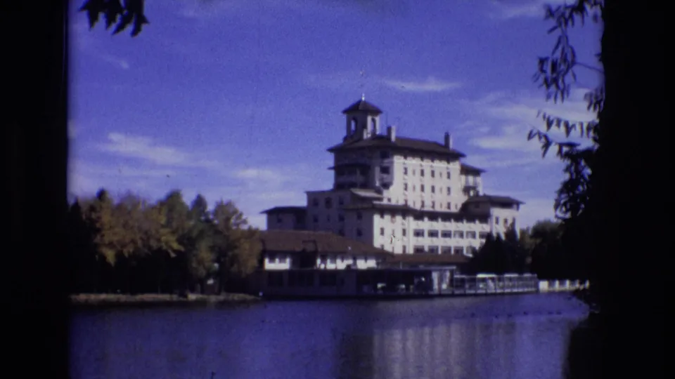 The Broadmoor Hotel stands across the lake in a 1974 Colorado Springs travel shot, with water reflections, trees, and dark foreground foliage visible.
