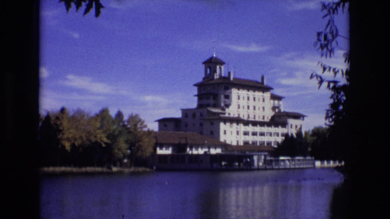 Lakeside hotel and bell tower framed by dark tree silhouettes.