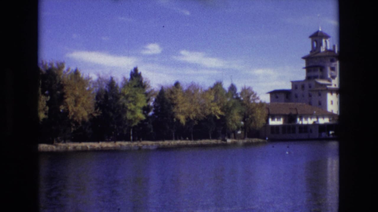 1974 Colorado Springs 8mm frame showing a large towered building partly visible across a calm lake behind a line of autumn trees.