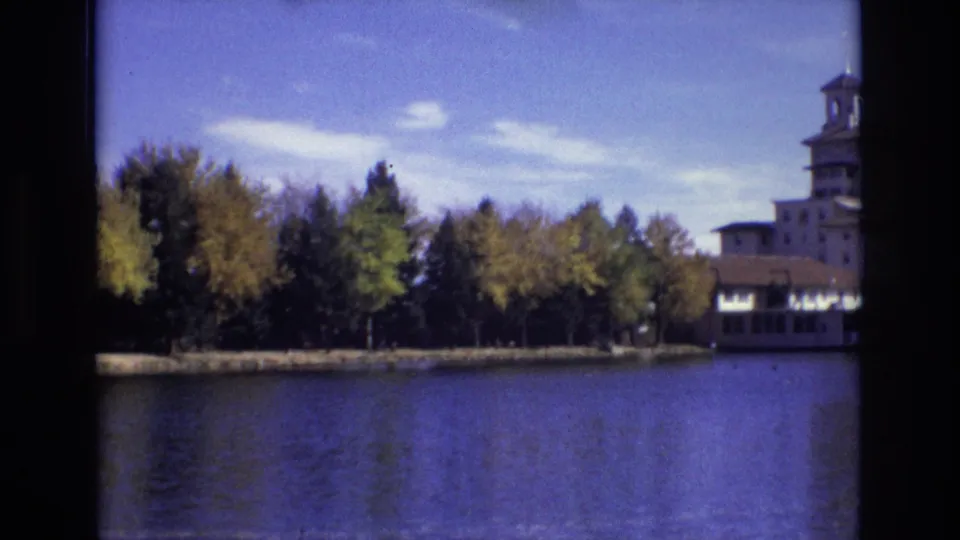 8mm Colorado Springs lakeside view from 1974, with autumn trees reflected near the shore and the towered building partly cropped at right.