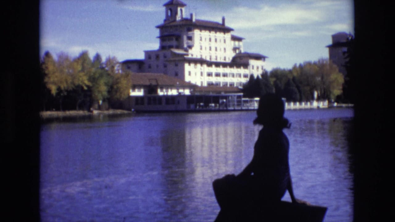 Silhouetted woman seated beside a lake with a large hotel across the water.