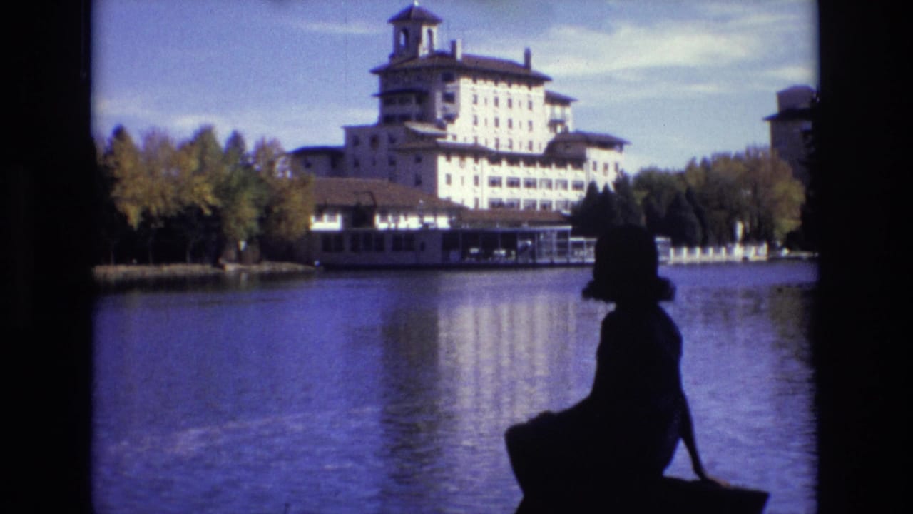 Backlit seated woman at the water's edge with a hotel reflected in the lake.
