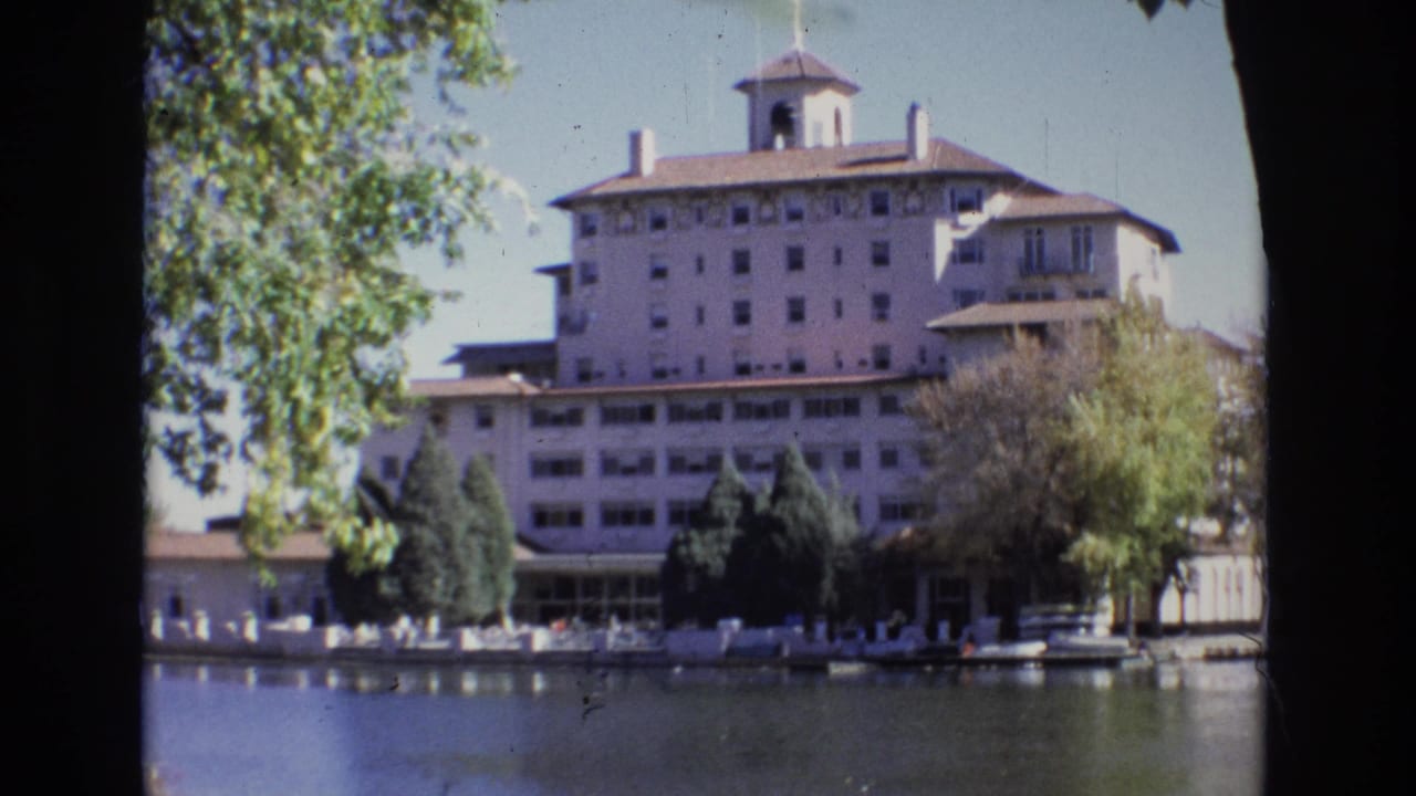 1974 Colorado Springs home-movie frame showing the Broadmoor Hotel across calm water, with trees framing the multi-story facade and cupola.