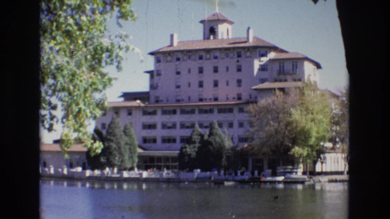 1974 Colorado Springs frame with the Broadmoor Hotel centered behind a treed waterfront, shot from across a calm waterway.