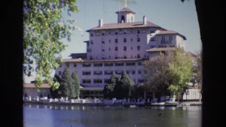 1974 Colorado Springs frame with the Broadmoor Hotel centered behind a treed waterfront, shot from across a calm waterway.