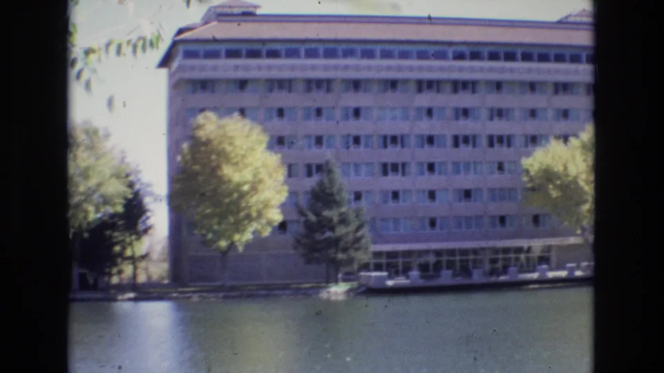 1974 Colorado Springs frame showing the Broadmoor Hotel wing across the water, with tree cover, window rows, and visible 8mm film texture.