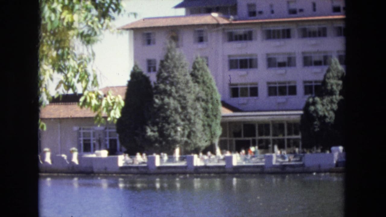 Hotel frontage, trees, and patio area reflected beside still water.