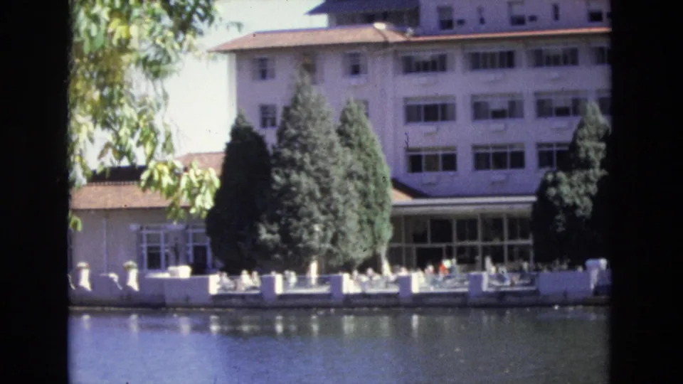 1974 Colorado Springs 8mm frame with the white hotel, red rooflines, evergreen trees, and waterside patio furniture under bright sun.