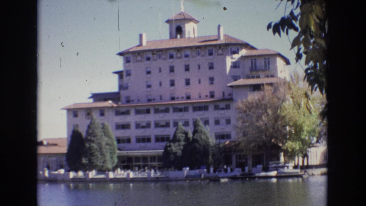 Large hotel building reflected near a lake edge with trees in front.
