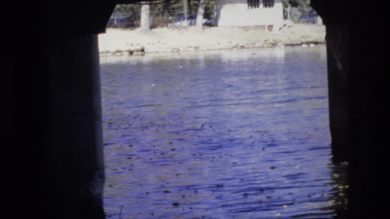 Rippling water seen between dark concrete bridge supports with a pale bank beyond.