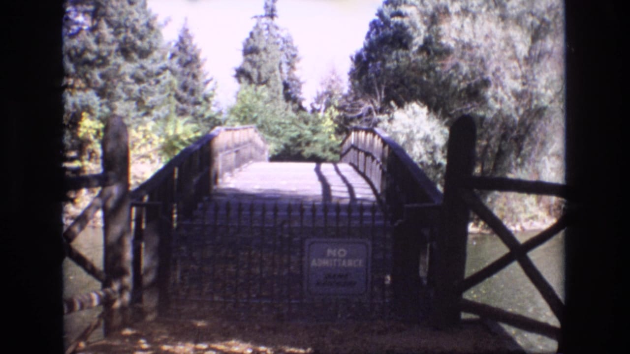 Rustic bridge framed by wooden railings, trees, water, and a no-admittance sign.