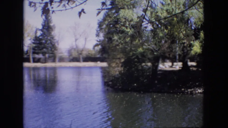 1974 Colorado Springs frame looking across still water toward trees and a small wooded shoreline point near the stadium area.