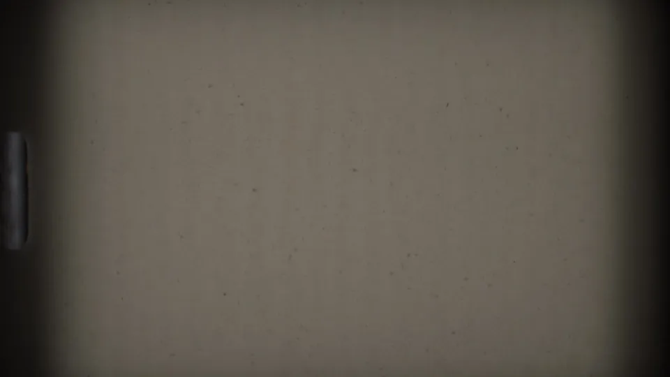 Opening frame from the 1974 Denver 8mm clip, with a large blank or obstructed film area and a partial glimpse of lawn, trees, cars, and a civic building at the right edge.