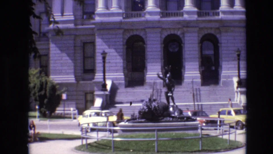 1974 Denver view of the building frontage with arched doorways, steps, a dark statue, yellow taxis, railings, and pedestrians at street level.