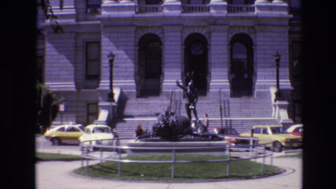 Bronze statue and stone building steps with parked cars in front.