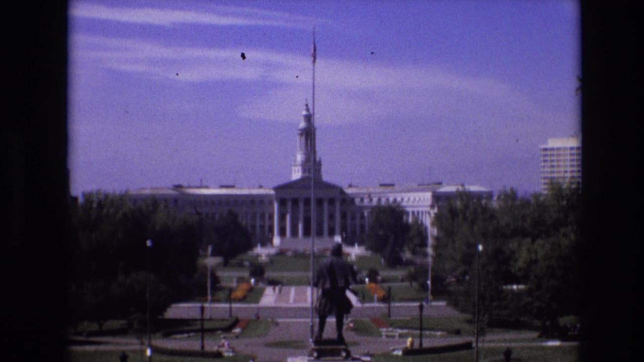 Wide view of the Colorado State Capitol beyond a foreground statue and park walkways.