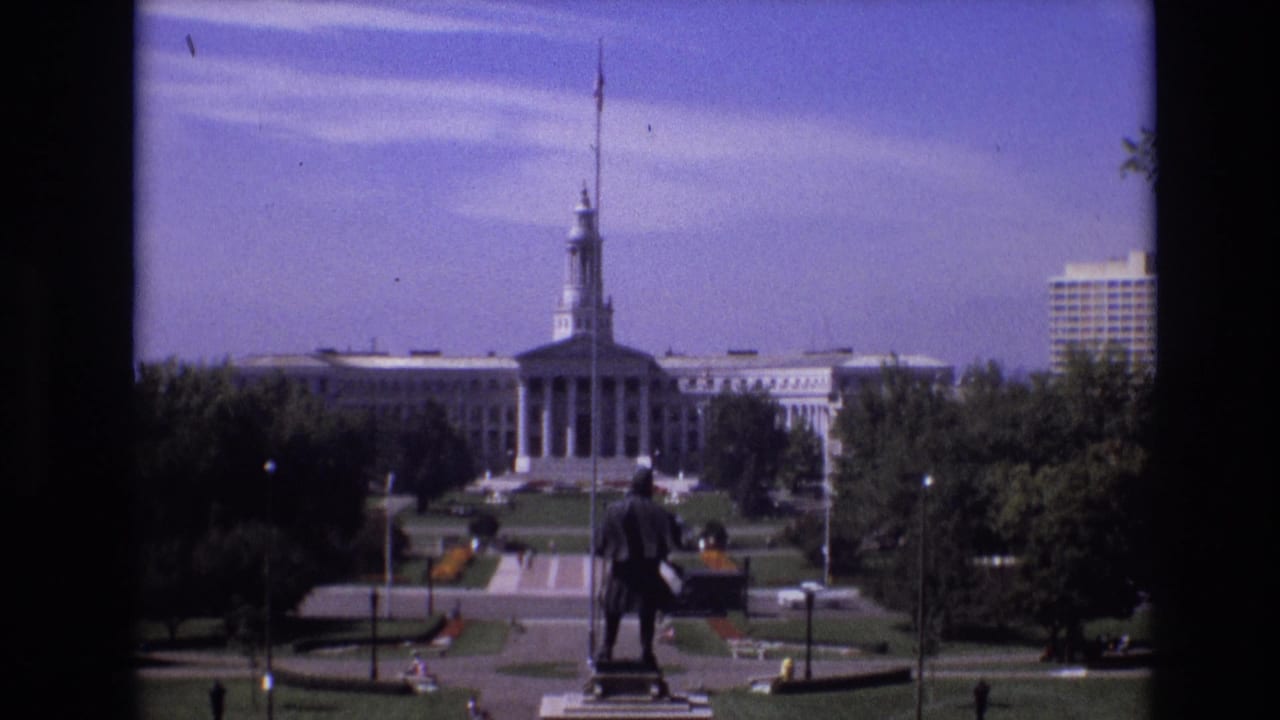 Capitol building seen across lawns and paths, with a statue centered in the foreground.