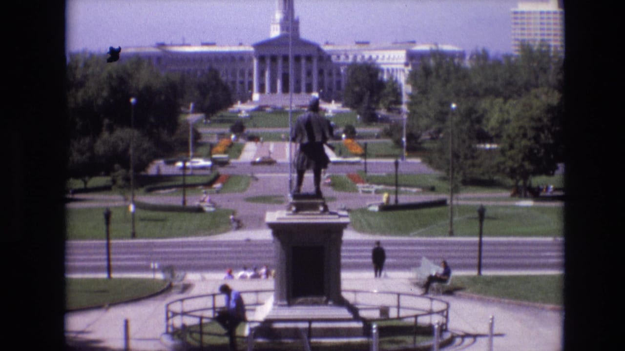 Closer view of a statue on a pedestal with a civic building and park paths behind it.