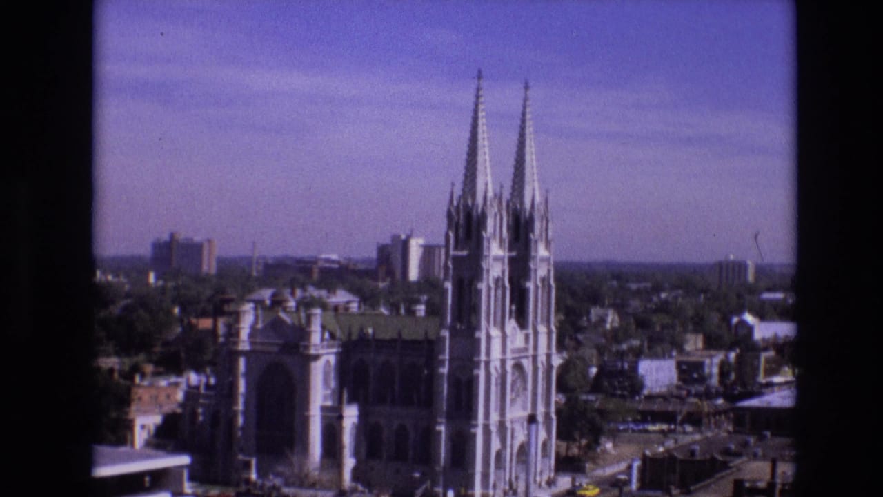 Elevated 1974 Denver view of a large Gothic-style cathedral with twin spires, rooftops, and distant city buildings under daylight.