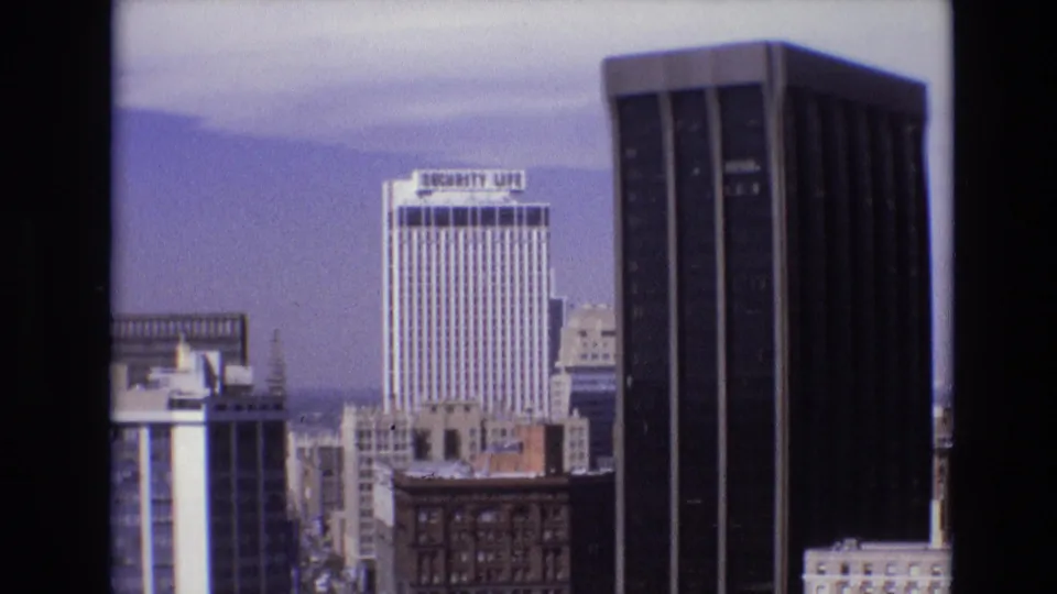 1974 Denver downtown skyline view with the Security Life building, neighboring high-rises, older masonry buildings, and pale blue sky.