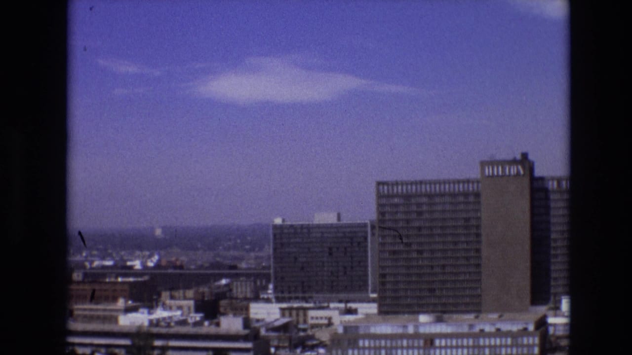 1974 Denver skyline view with rectangular high-rise buildings and a prominent hotel-like tower seen from an elevated home-movie viewpoint.