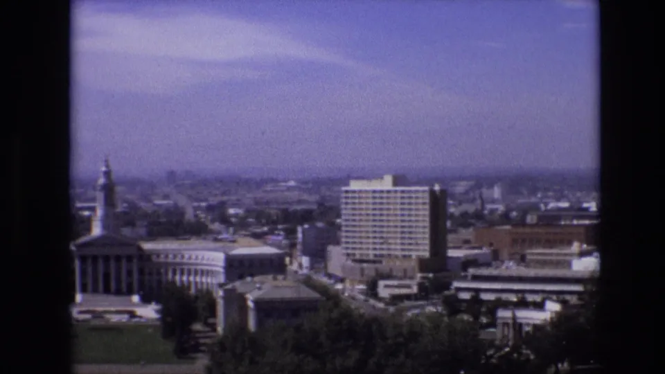 1974 Denver city view with a columned civic building in the foreground, open grass and trees, and modern high-rise buildings behind it.