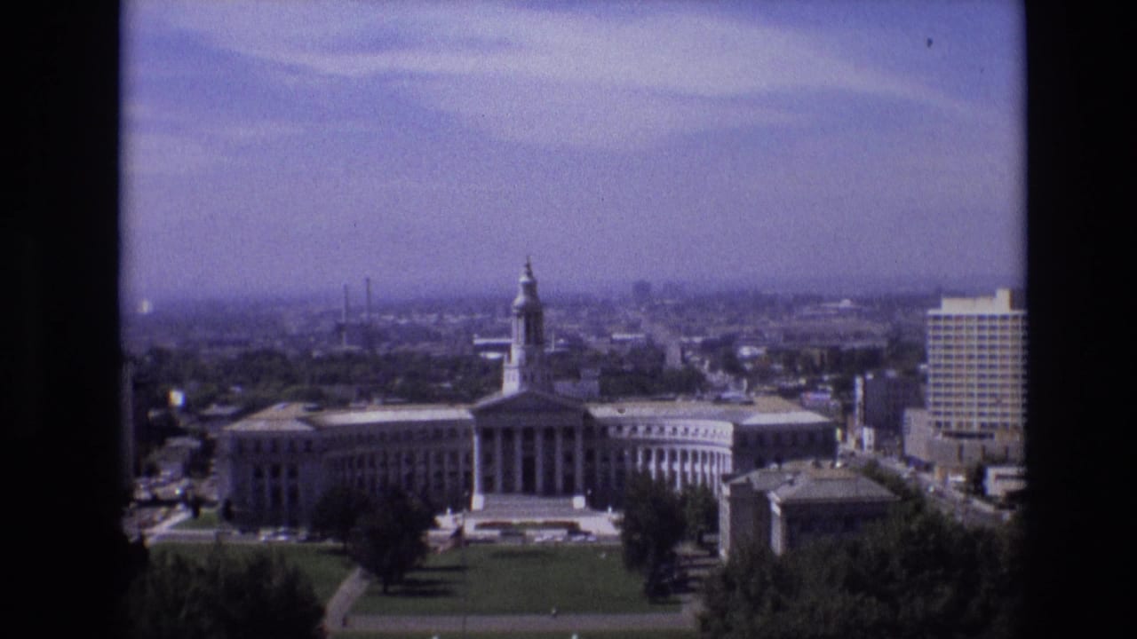 Wide elevated view of the same towered classical building, lawn, trees, and a high-rise at right.