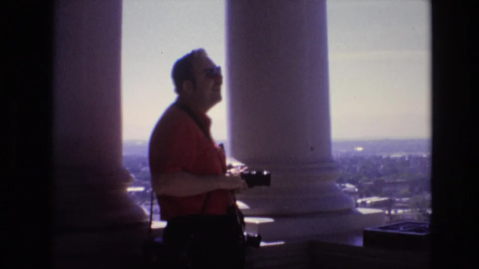 At the Denver overlook in 1974, the man remains in profile beside the columns, holding his camera as the bright skyline appears beyond the terrace.