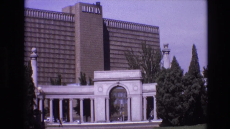 1974 Denver frame showing the Hilton-branded hotel tower and the pale colonnaded entrance framed by trees and 8mm film borders.